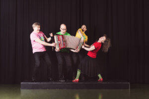 Kuva Loiskis – lastenmusiikkiorkesterista. Neljä henkilöä lavalla, jotka vetävät harmonikkaa auki.