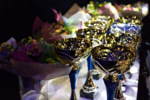 Lähikuva palkintopöydästä, jossa pokaaleita ja taustalla kukkia.