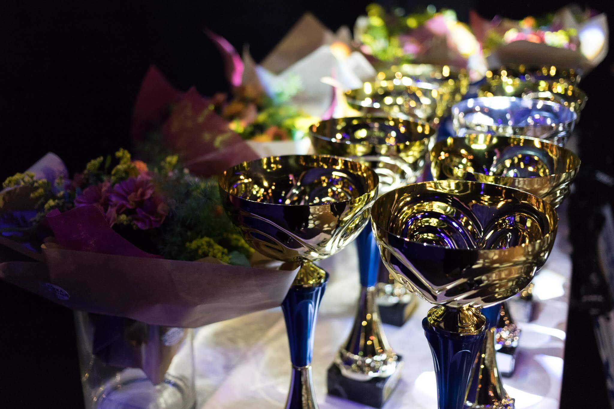 Lähikuva palkintopöydästä, jossa pokaaleita ja taustalla kukkia.