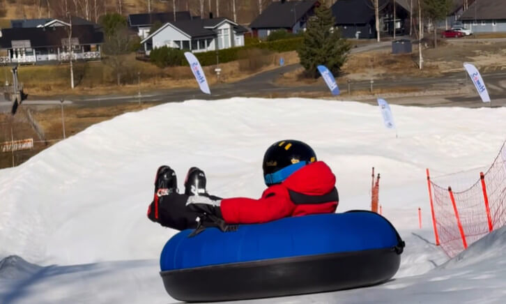 henkilö laskee lumista rinnettä alas sinisellä donitsi-mallisella välineellä.