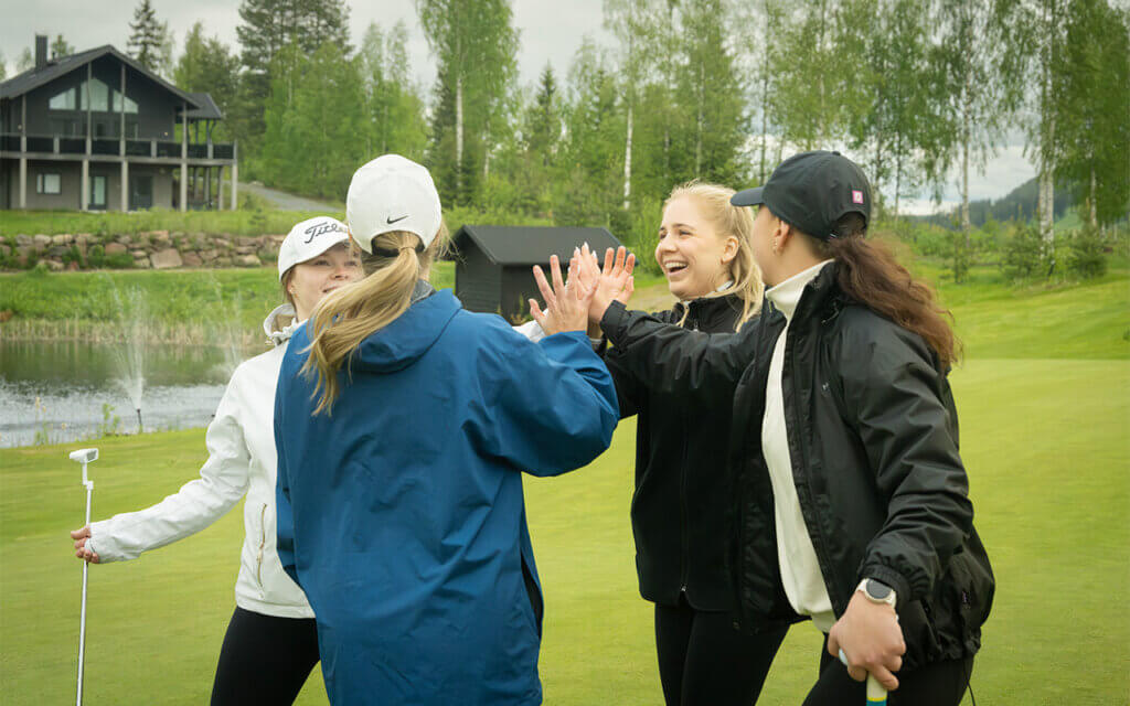 Neljä henkilöä hymyilee ja lyövät ylävitosia golfkentällä HImoksella.