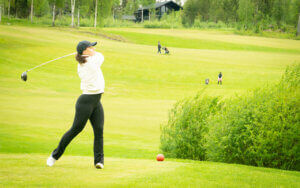 Vaaleaan paitaan ja tummiin housuihin pukeutunut pitkähiuksinen golffari, joka on juuri lyönyt palloa Himoksen golfkentällä .