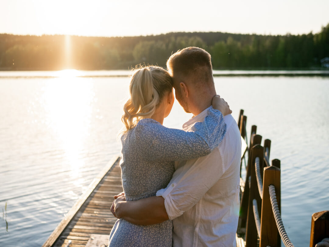 Kaksi henkilöä syleilevät toisiaan järven rannalla iltaauringon paisteessa laiturilla Himoksella.