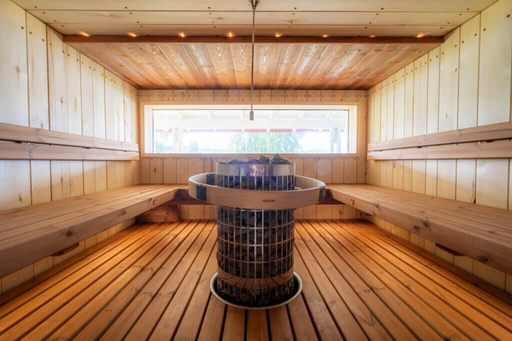 Puinen sauna, jonka keskellä iso harvia-merkkinen kiuas. Ikkuna, josta näkyy vihreää.