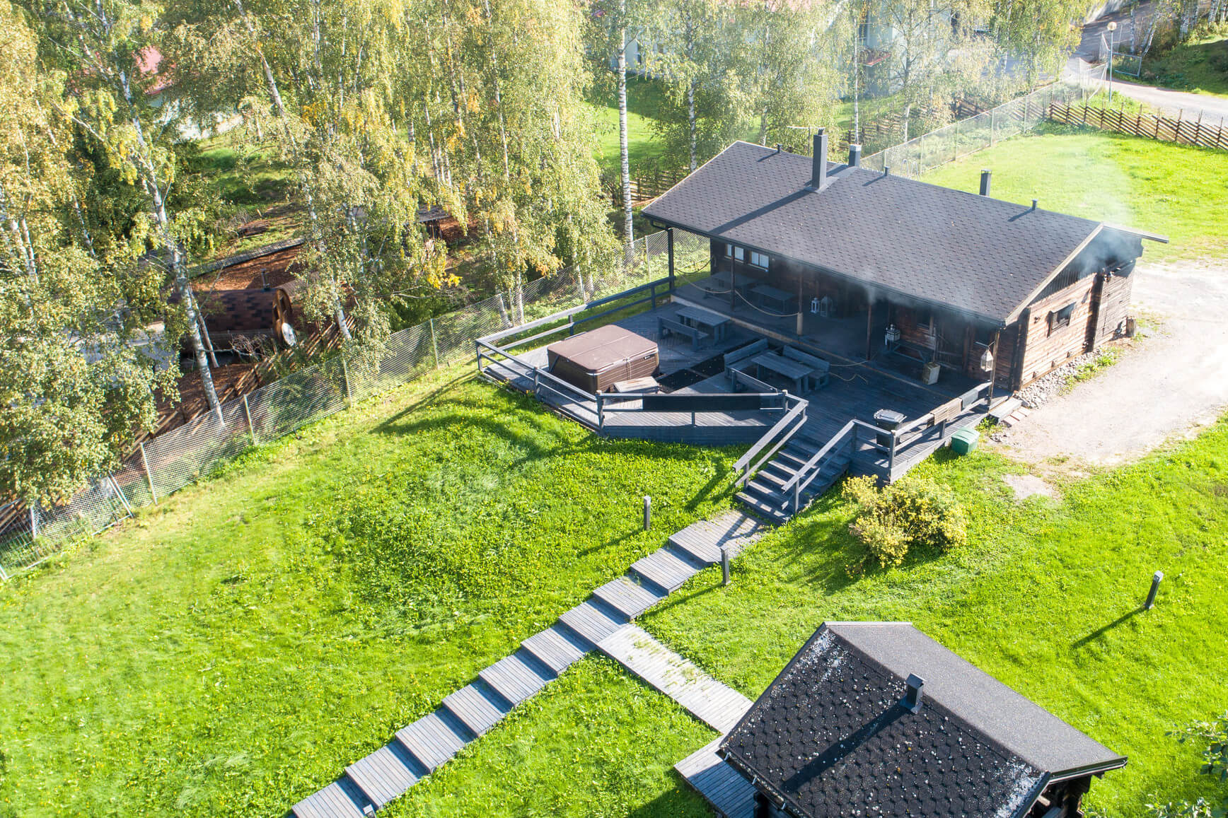 Kesäinen ilmakuva Himoksen Saunapihasta, kuvassa näkyy savusauna, jota lämmitetään. Pitkät puiset portaat vievät saunalta alas.