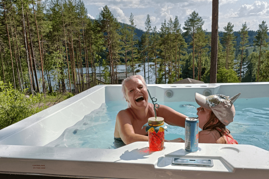 Aikuinen ja lapsi ilakoivat ulkoporealtaassa Himoksella kesällä. Altaan laidalla on juomia, aurinko paistaa ja on vihreää.