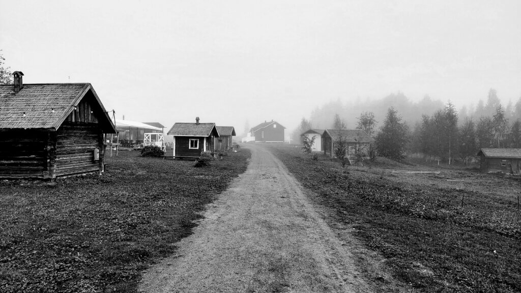 Mustavalkoinen kuva Jämsän saunakylästä, jossa vanhoja savusaunoja hämyisessä tunnelmassa.