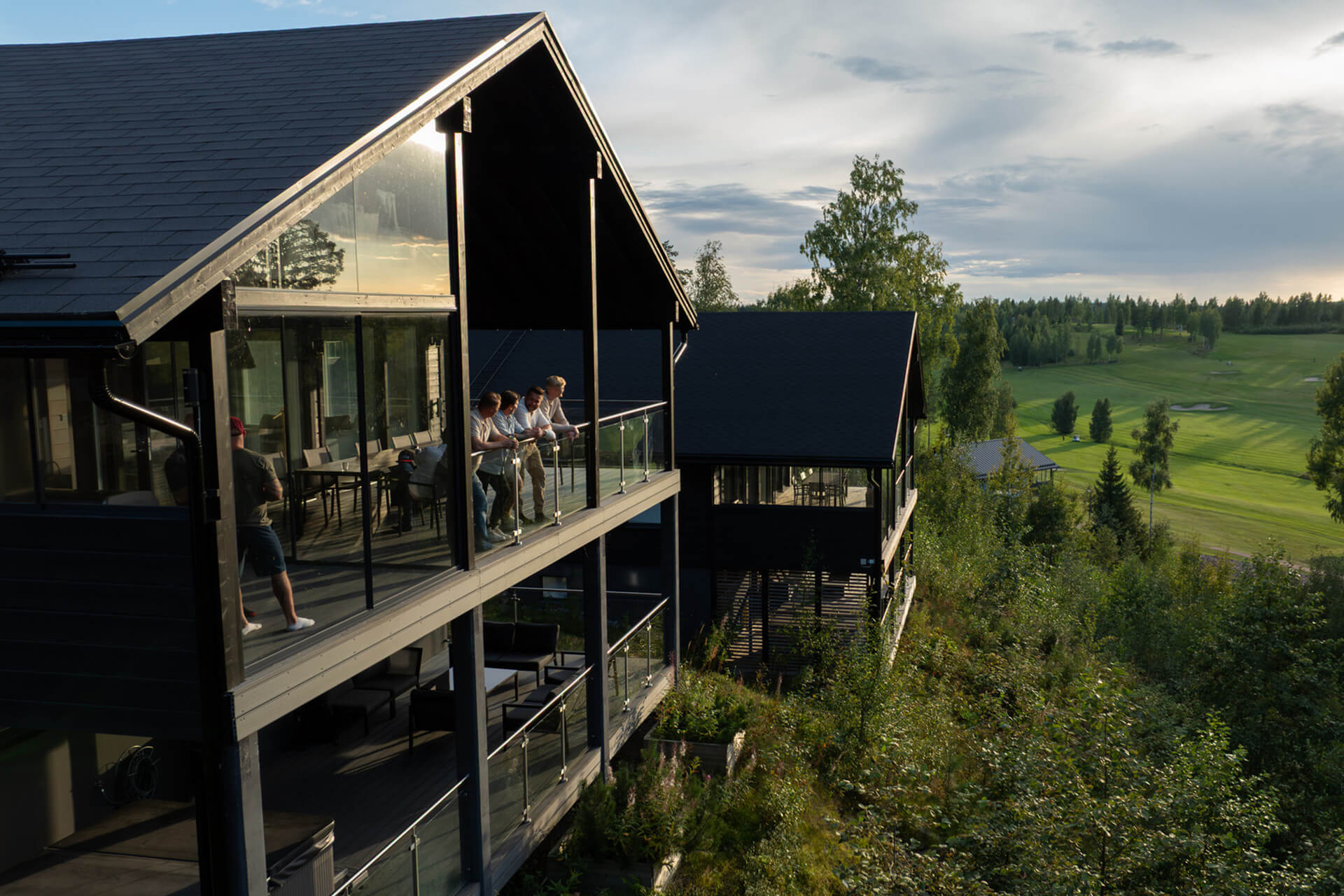 Ihmisiä nojaa kaiteeseen Himoksen suuren huvilan terassilla. Taustalla näkyy vihreä golfkenttä.