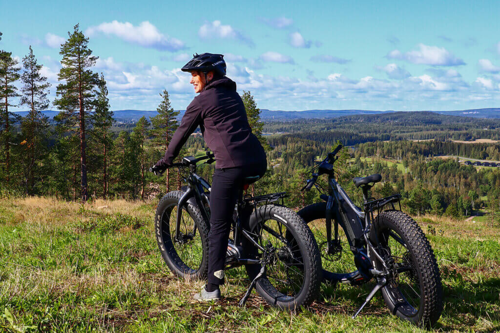 Kaksi fatbike-pyörää rinteiden päällä ja taustalla kaunis kesäinen maisema näkyvillä.