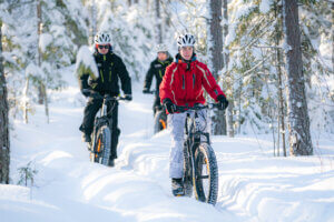 Sähkökäyttöisillä fatbikeilla kulkemassa ihmisiä lumisessa metsässä tehtyä polkua pitkin.