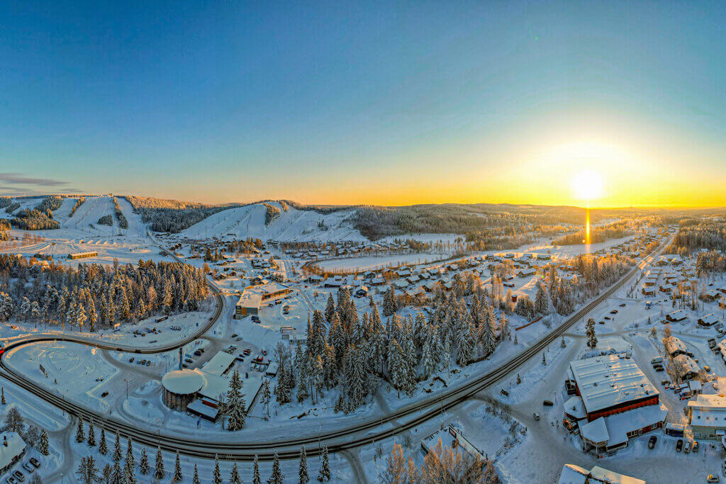 Talvinen ilmakuva Himoksen alueesta; ravintoloista ja mökkikylistä, ja taustalla auringonlasku ja Himoksen länsirinteet.