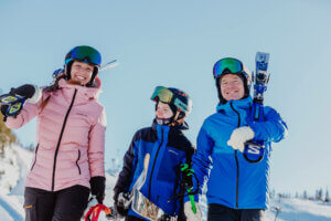 Laskettelijaperhe kulkemassa sukset olalla hymyillen. Kuva: Himos hiihtokeskus.