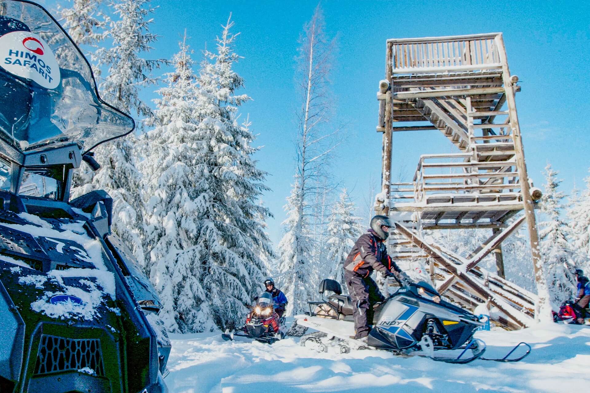 Moottorikelkkailijoita saapumassa Morvan näköalatornille lumisten puiden ympäröiminä.