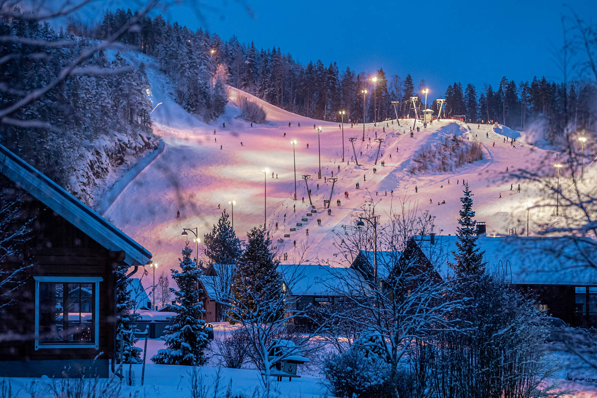 Talvinen tunnelma Länsi-Himoksen mökkikylästä, jossa taustalla näkyy Himoksen länsirinteet ja laskettelijoita.