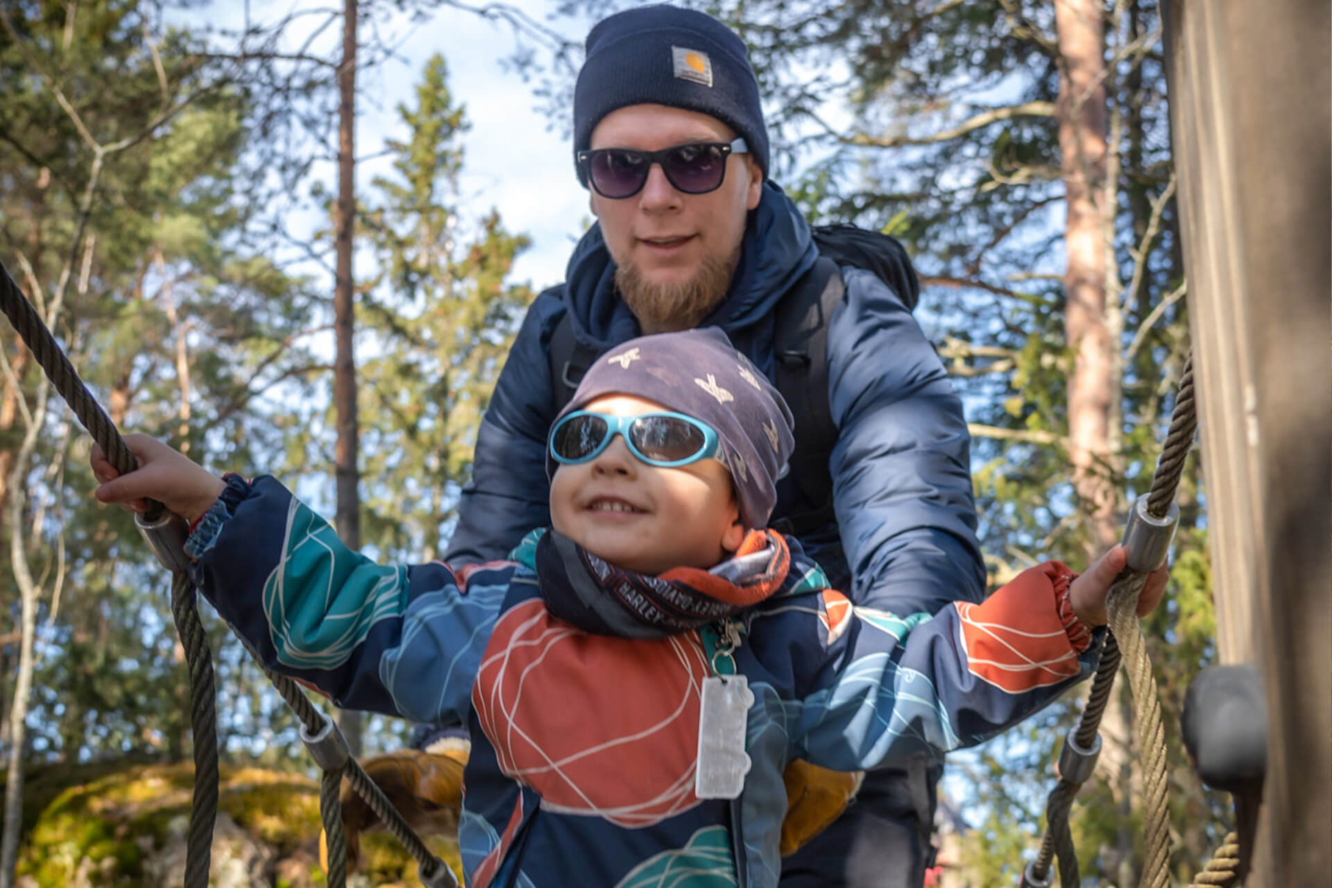 Isä ja poika kiipeilee riippusillalla syksyisissä maisemissa.