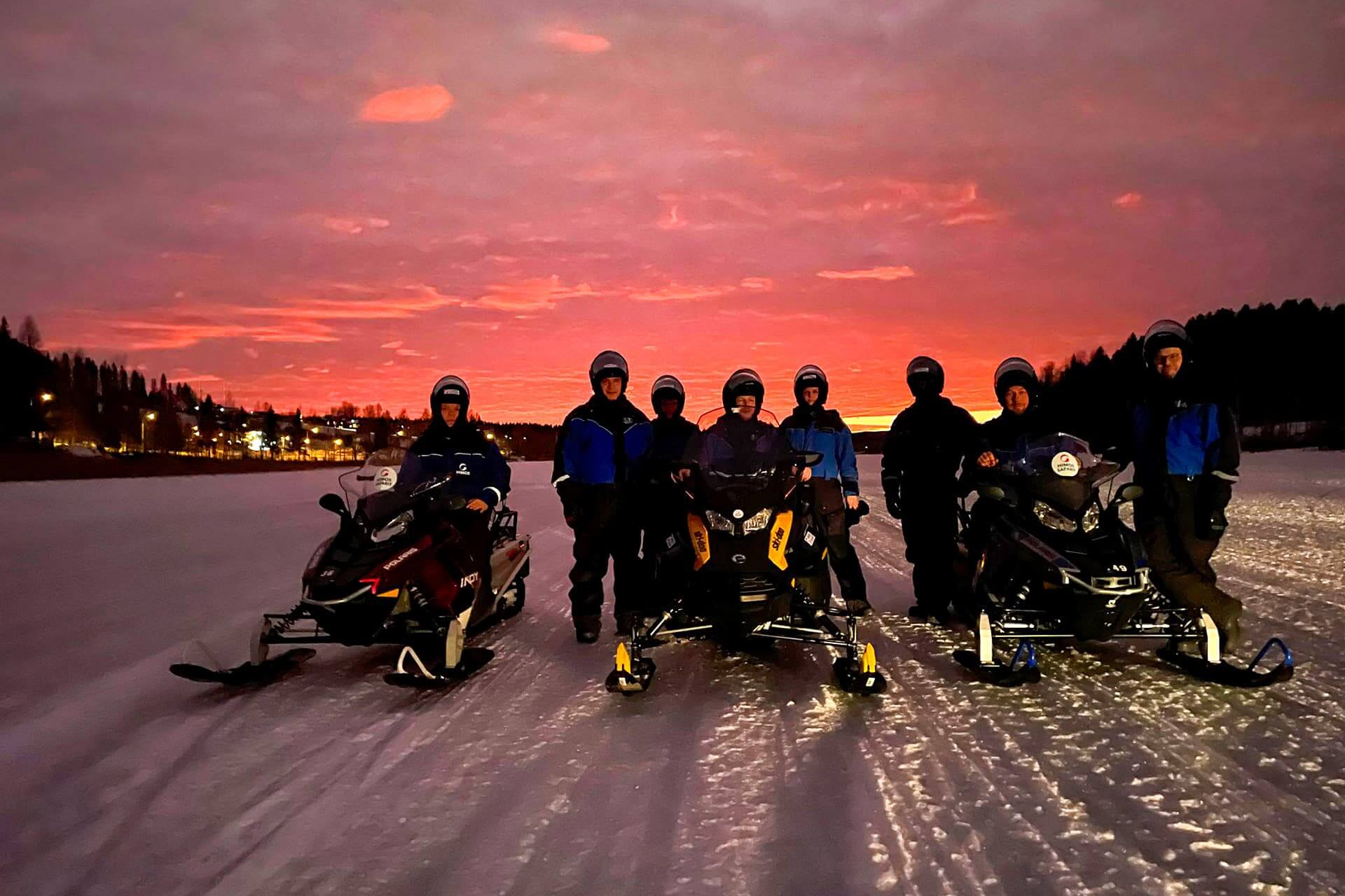 Ryhmä moottorikelkkailijoita Himoksen Patalahden jäällä auringon laskun aikaan. Taivas on punainen, on ilta.