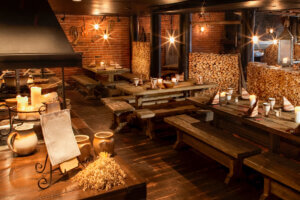 Tyhjä ravintola, jossa on puiset pöydät, rustiikkinen miljöö ja punatiilinen seinä.