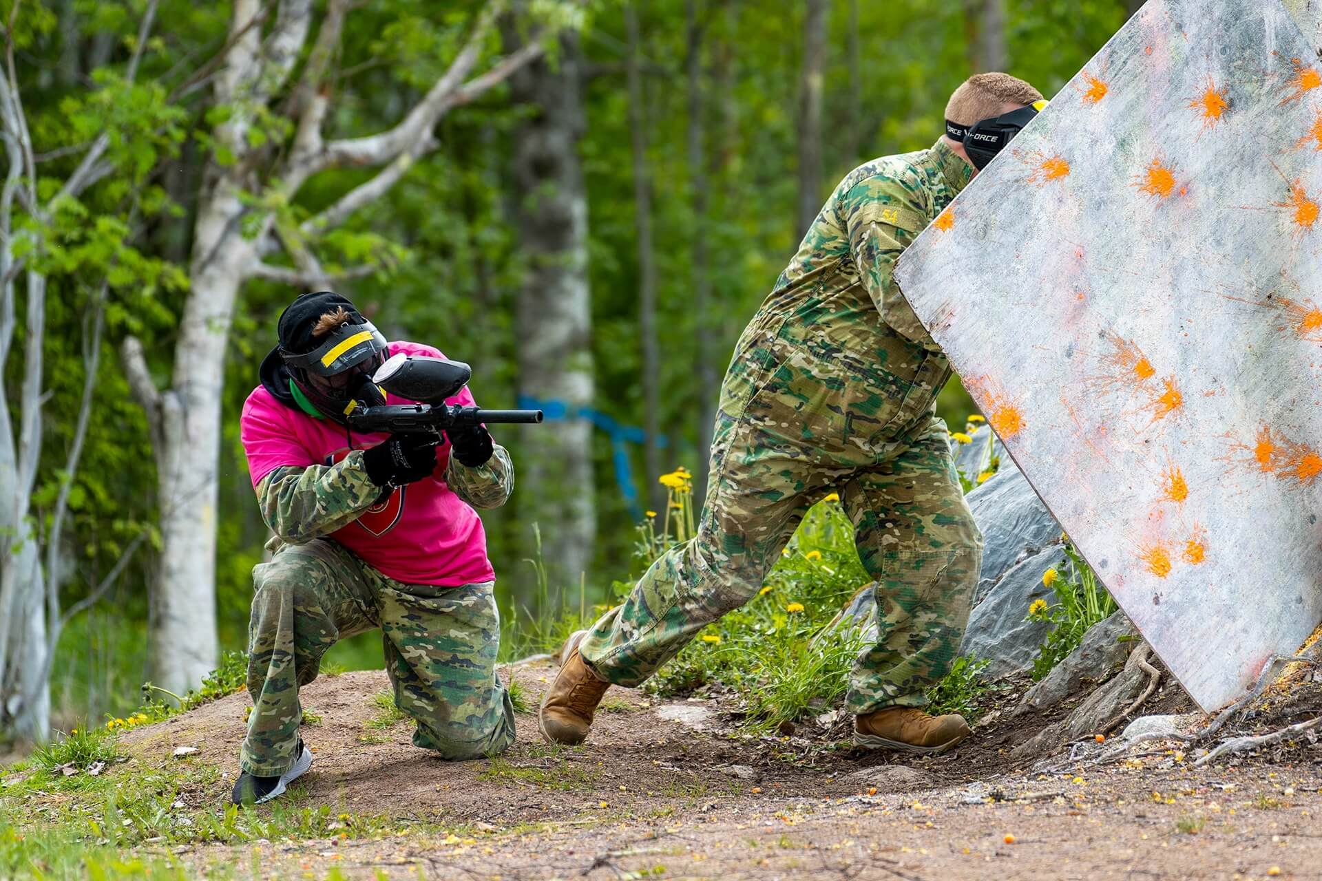 Kaksi henkilöä pelaa paintballia, eli värikuula-asepeliä.