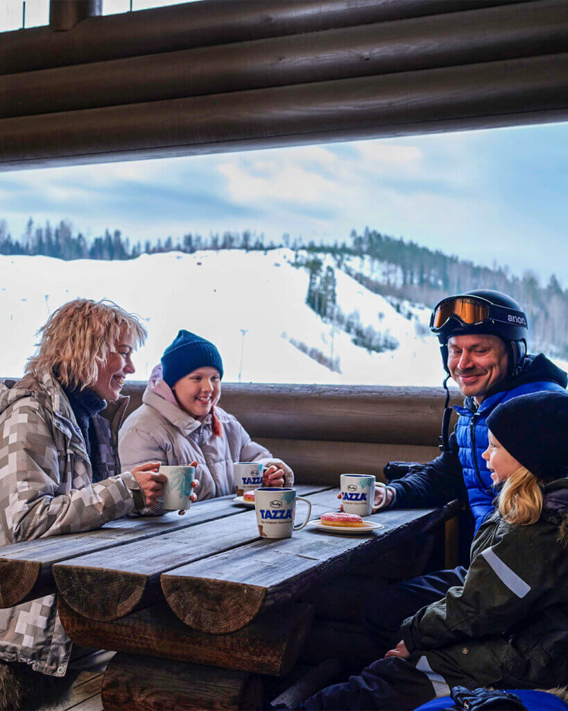 Perhe nauttimassa kuumia juomia rinneravintolassa.